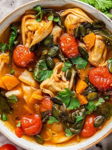A bowl of vegan tortellini soup with fresh parsley on top.