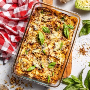 Freshly baked vegan cabbage lasagna in an oven dish surrounded by ingredients.