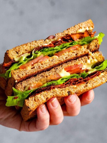 A hand holding a vegan BLT sandwich with carrot bacon.