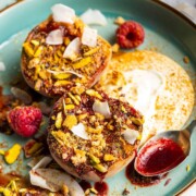 Grilled balsamic peaches with coconut yogurt and raspberry coulis on a dessert plate.