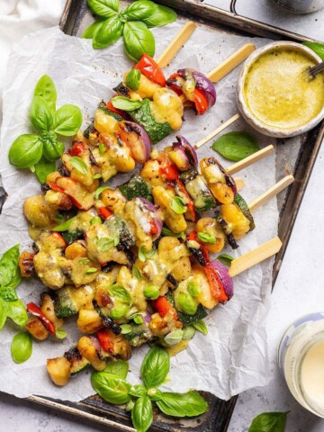 Vegan skewers with gnocchi and vegetables on a platter with pesto drizzle.