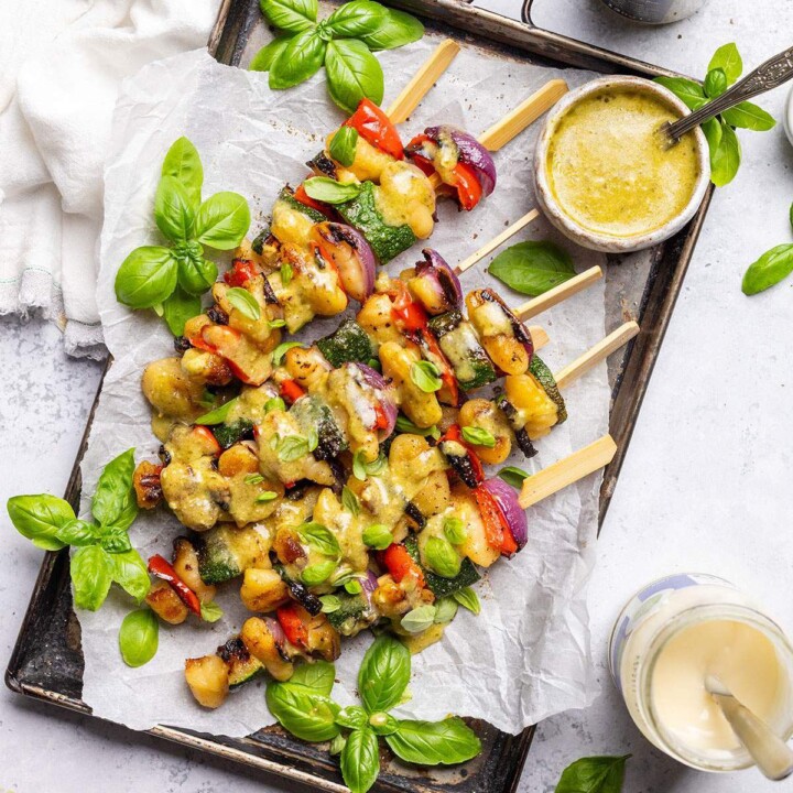 Vegan skewers with gnocchi and vegetables on a platter with pesto drizzle.