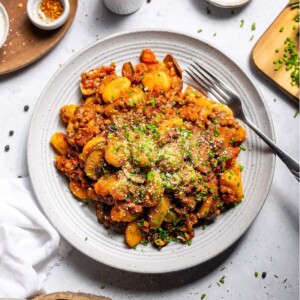Vegan gnocchi with hearty lentil ragu and fresh chives on a serving plate on the dinner table.