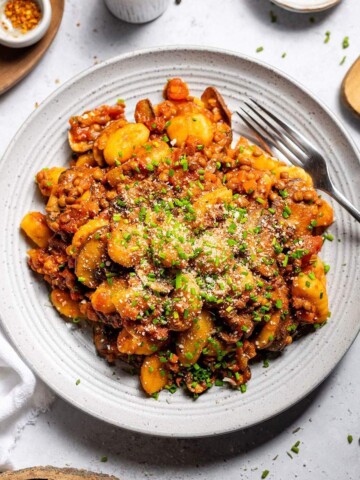 Vegan gnocchi with hearty lentil ragu and fresh chives on a serving plate on the dinner table.