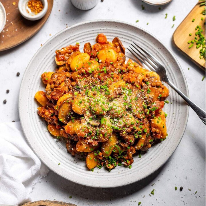 Vegan gnocchi with hearty lentil ragu and fresh chives on a serving plate on the dinner table.