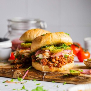 Two Vegan sloppy joes on a serving board with lentils and pickles.