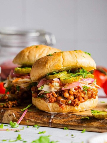 Two Vegan sloppy joes on a serving board with lentils and pickles.