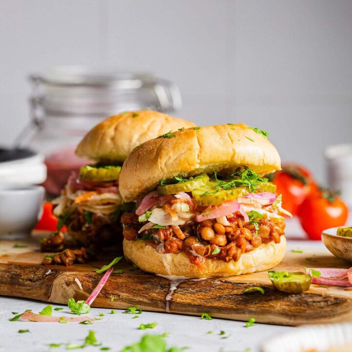 Two Vegan sloppy joes on a serving board with lentils and pickles.