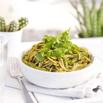 A bowl of green vegan spinach pasta with fresh arugula on top.