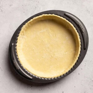 Vegan tart base in a tart tin on a white table.