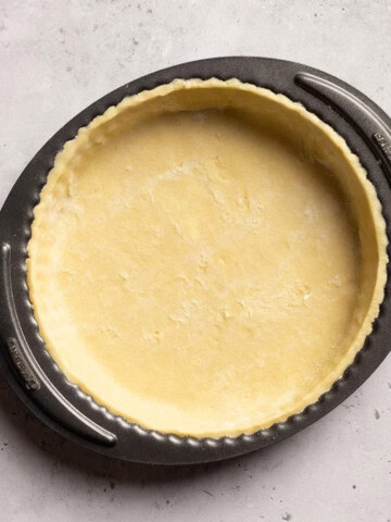 Vegan tart base in a tart tin on a white table.