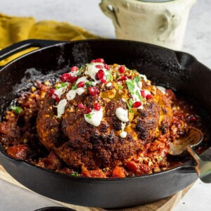 A whole roasted cauliflower in a cast iron skillet garnished with fresh pomegranate seeds.