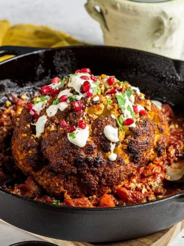A whole roasted cauliflower in a cast iron skillet garnished with fresh pomegranate seeds.