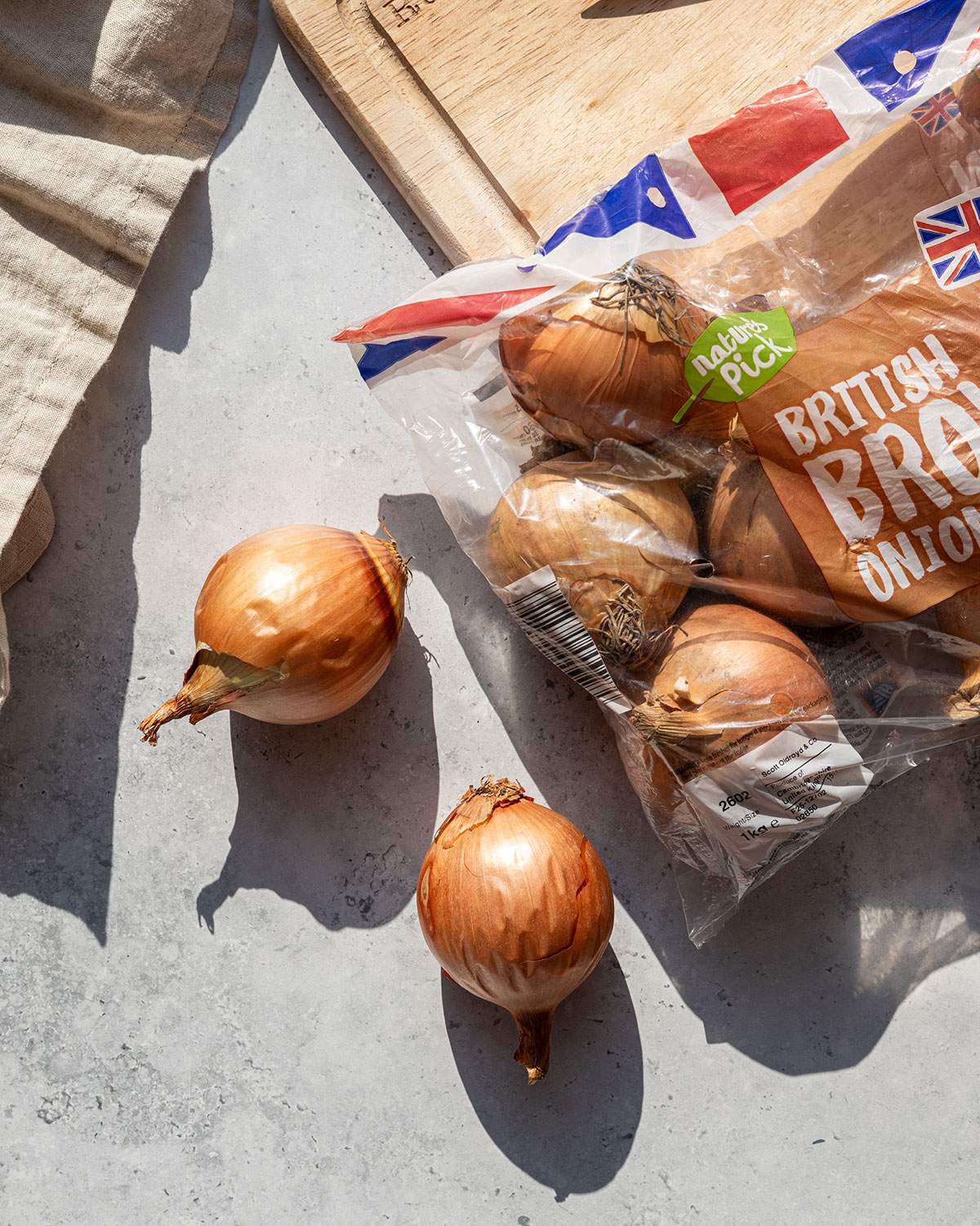 Several whole onions in and next to grocery packaging, with natural shadows.