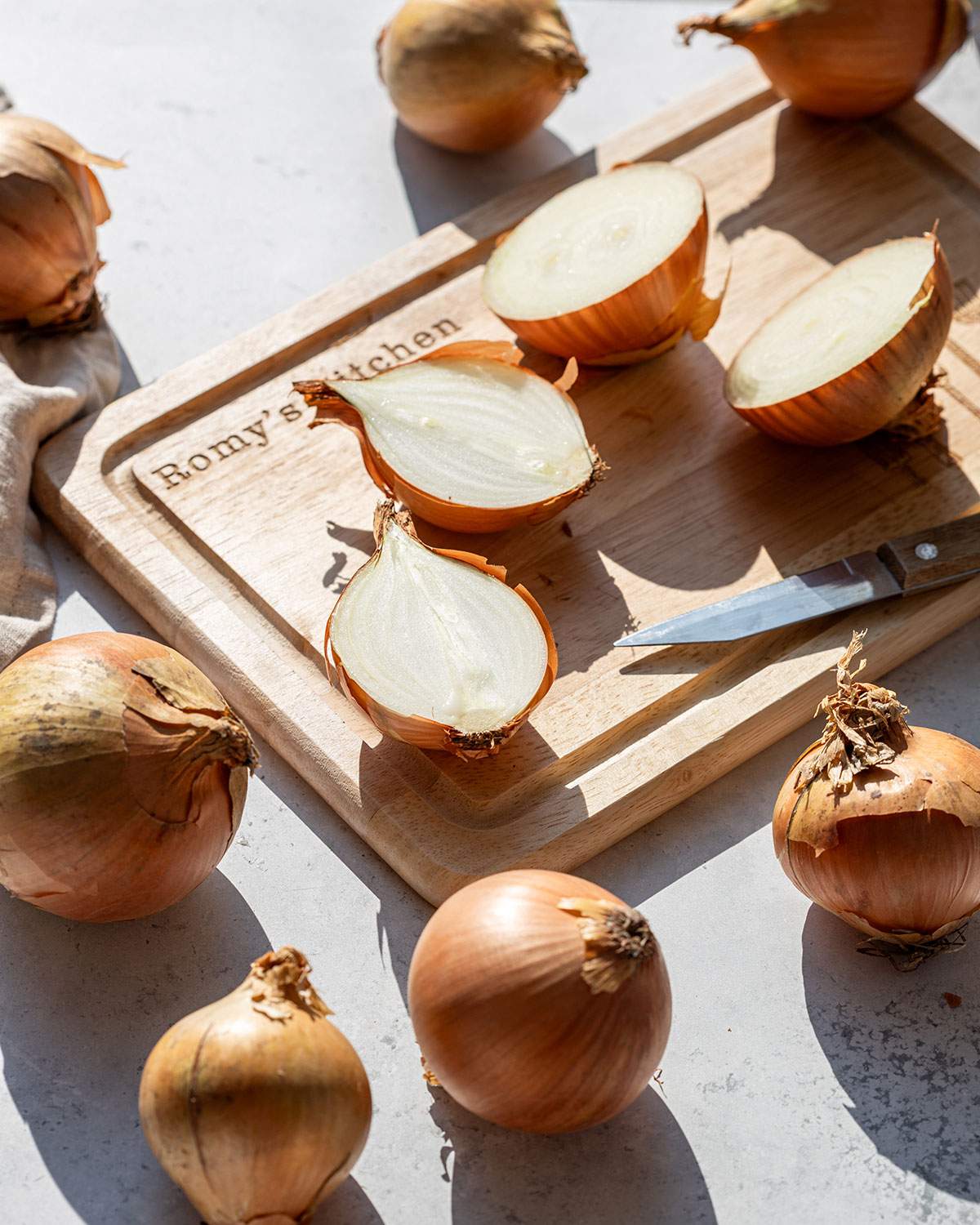 Sliced onions on a cutting board surrounded by whole onions, ready for cooking.