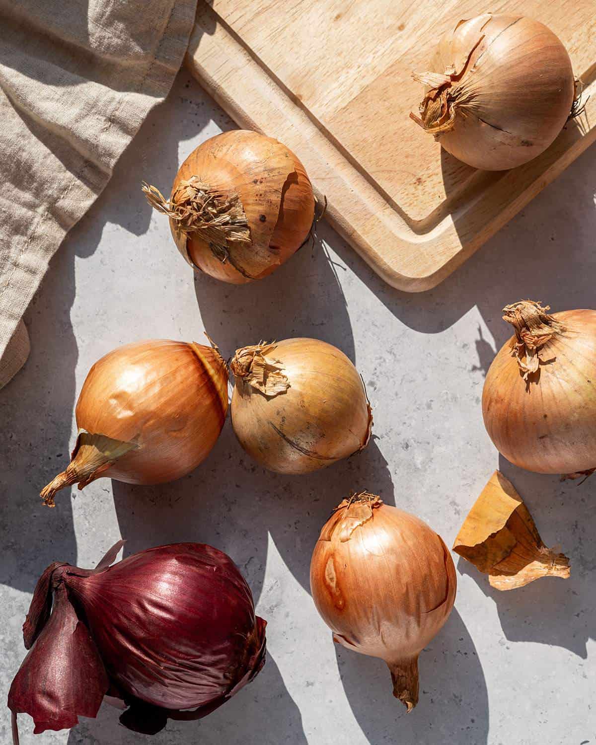 Yellow and red onions scattered with a wooden chopping board and tea towel.