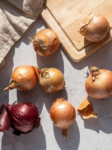 Mixed group of yellow and red onions laid out on a light stone surface.