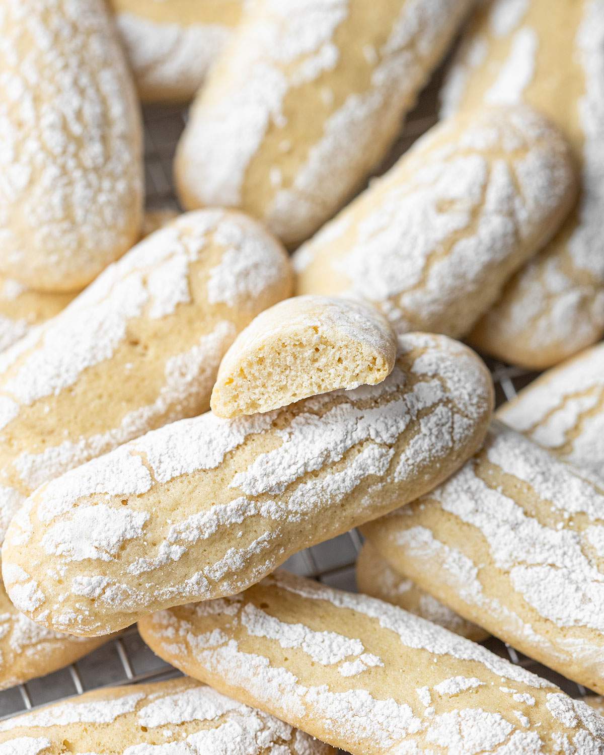 Vegan ladyfinger biscuits dusted with icing sugar, one biscuit showing the texture inside.