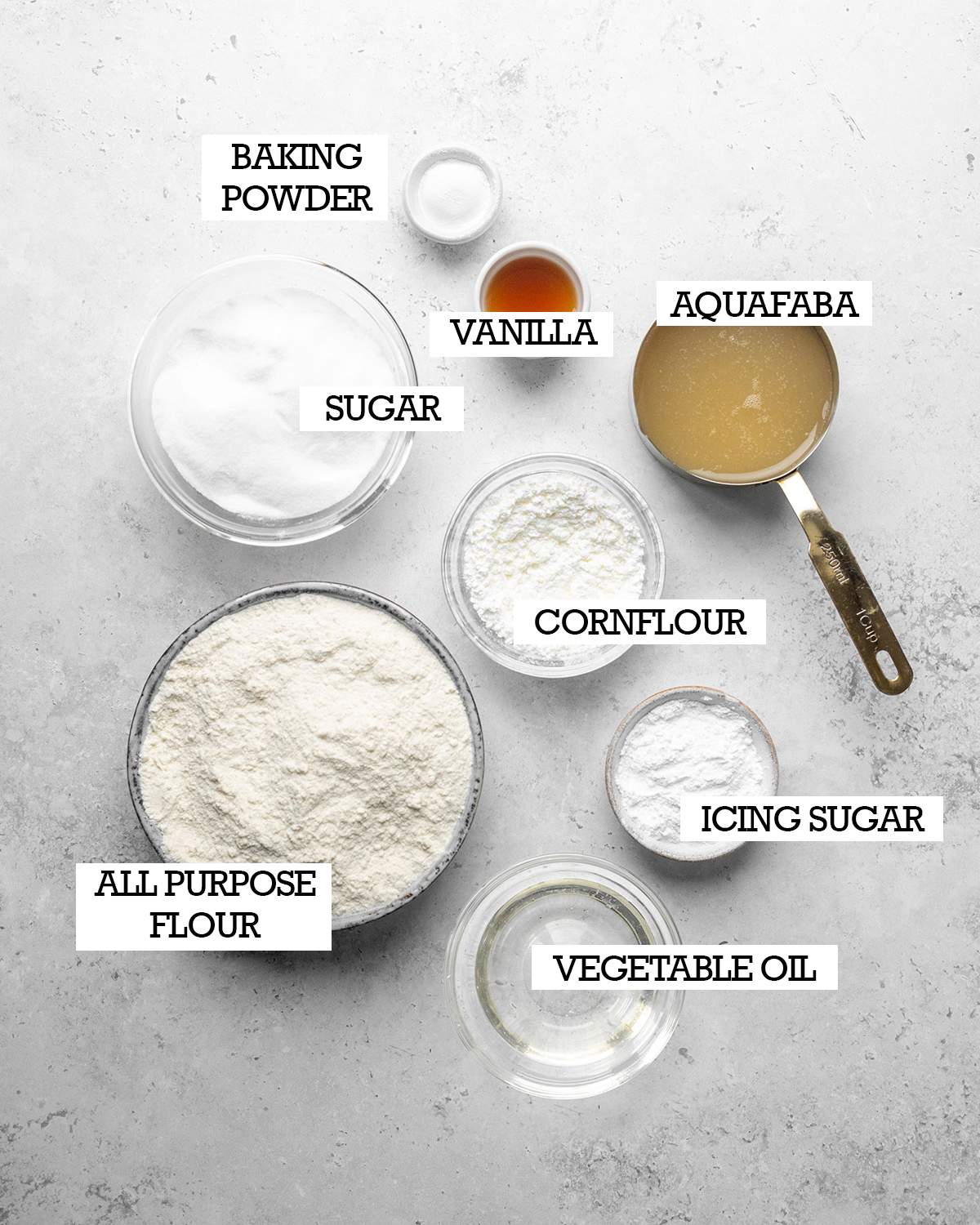 All ingredients for making vegan ladyfingers on a white kitchen surface with labels.
