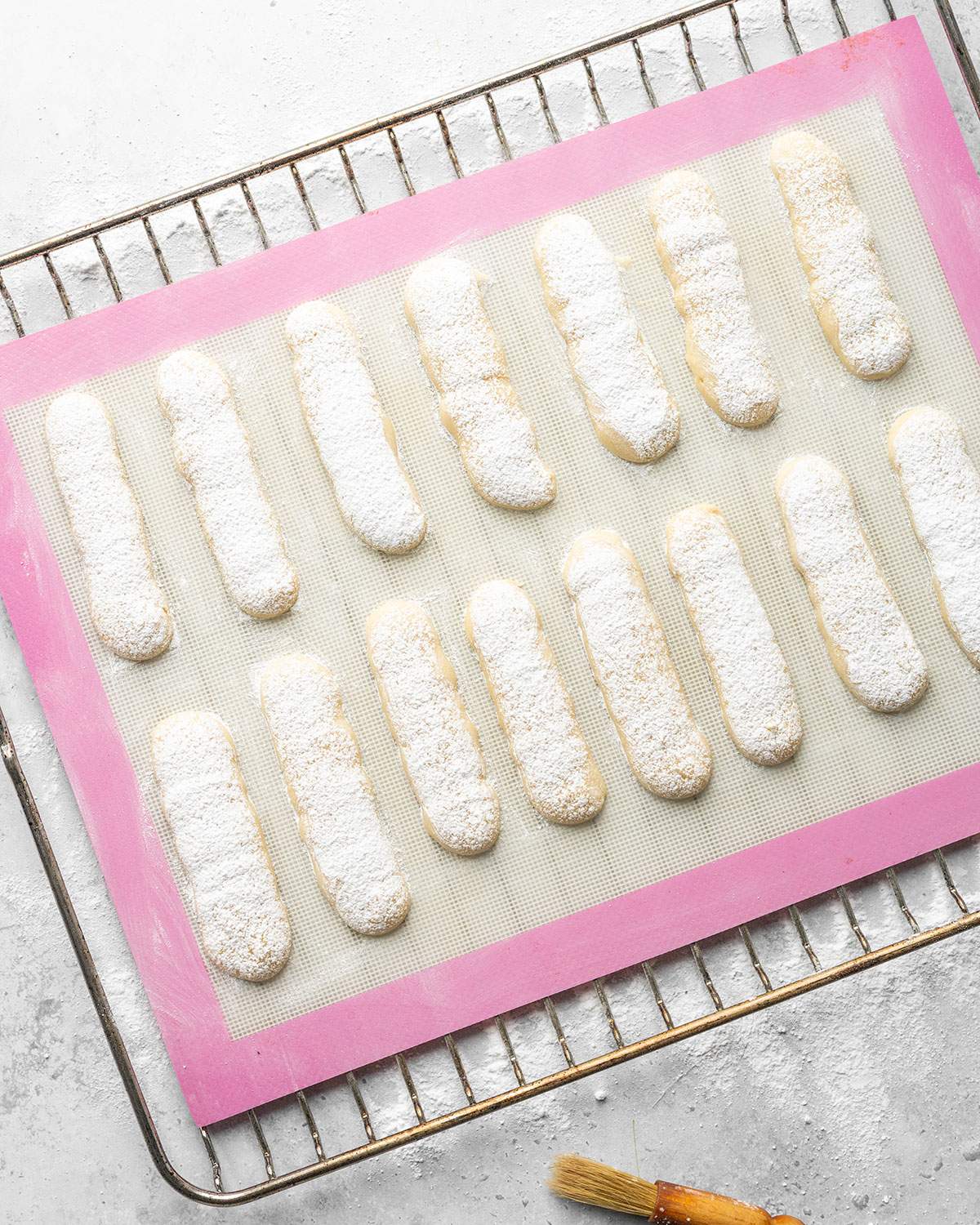 Shaped ladyfingers dusted with sugar on a baking sheet.