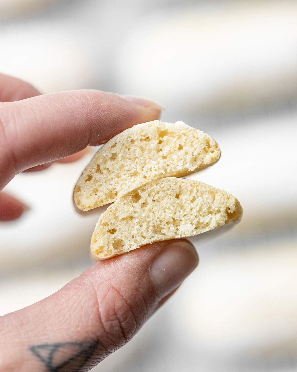 Hands holding a broken ladyfinger biscuit showing the texture inside.