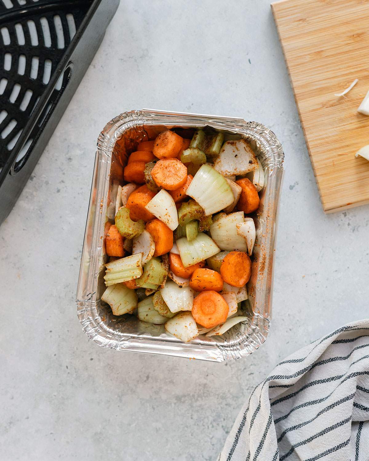 Food arranged in an aluminum pan next to an air fryer basket.