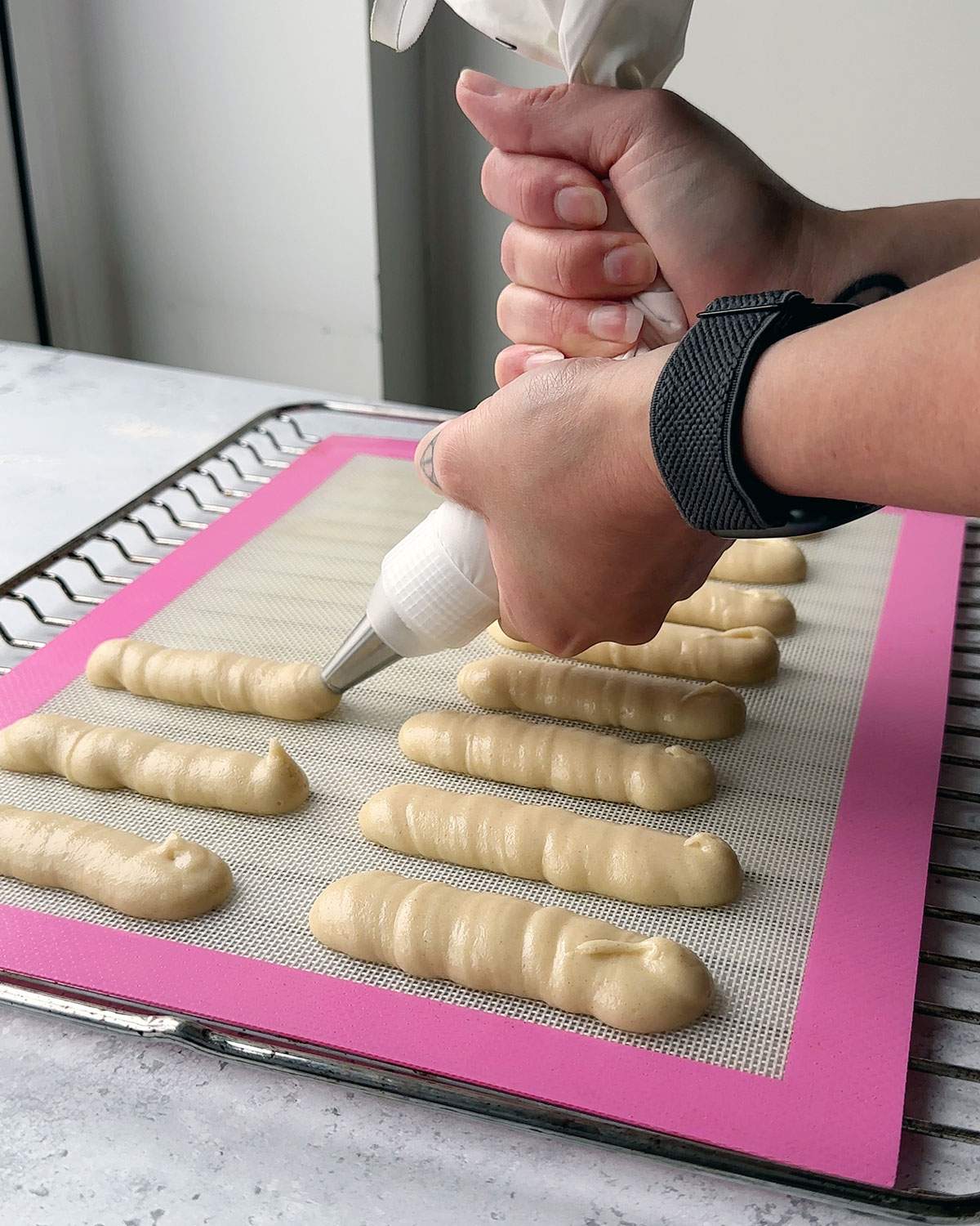 Piping ladyfinger biscuit batter onto a lined baking sheet.