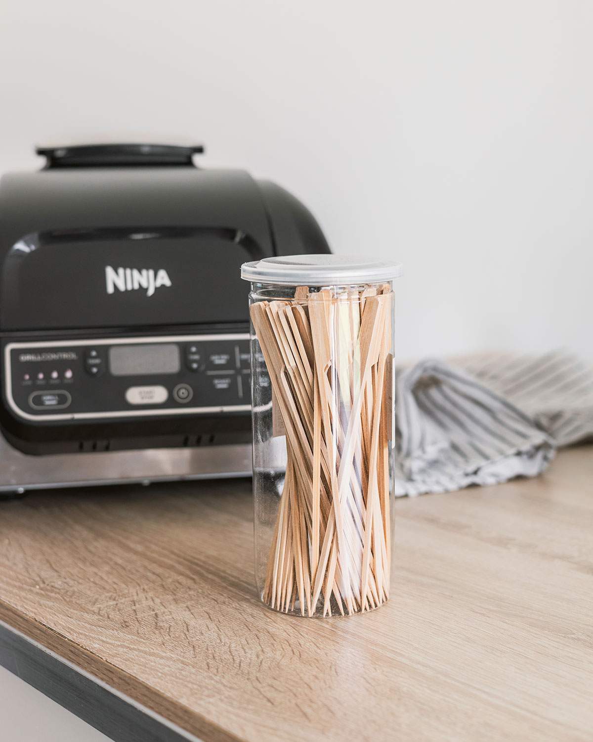 A jar of wood skewers on the kitchen counter in front of an air fryer.