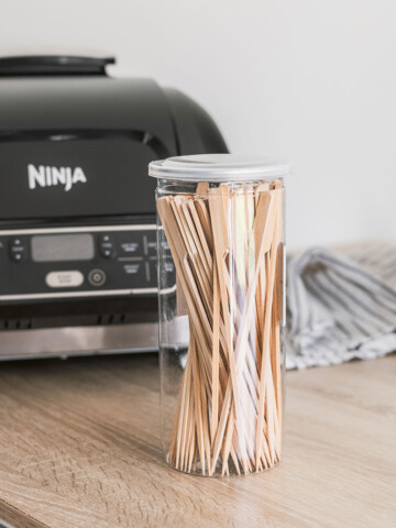 A jar of wood skewers on the kitchen counter in front of an air fryer.
