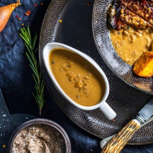 A gravy boat filled with a vegan peppercorn sauce next to a festive dinner.