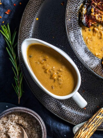 A gravy boat filled with a vegan peppercorn sauce next to a festive dinner.