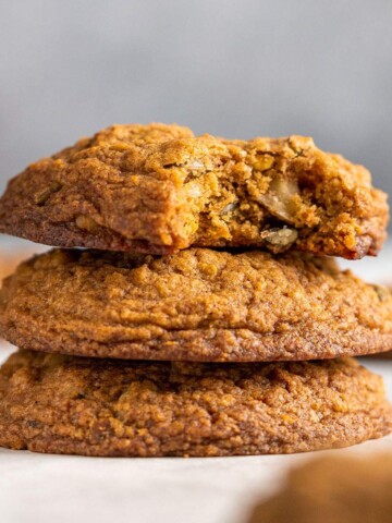 A stack of pumpkin cookies with a bite taken out of the top cookie.
