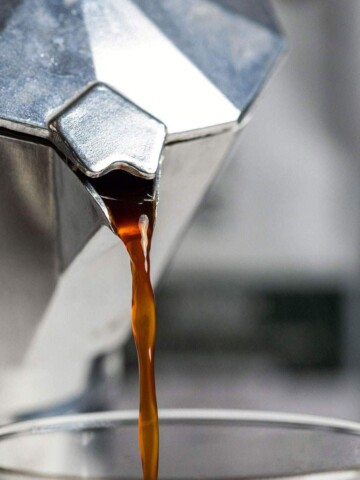 Freshly brewed coffee pouring out of a moka pot.