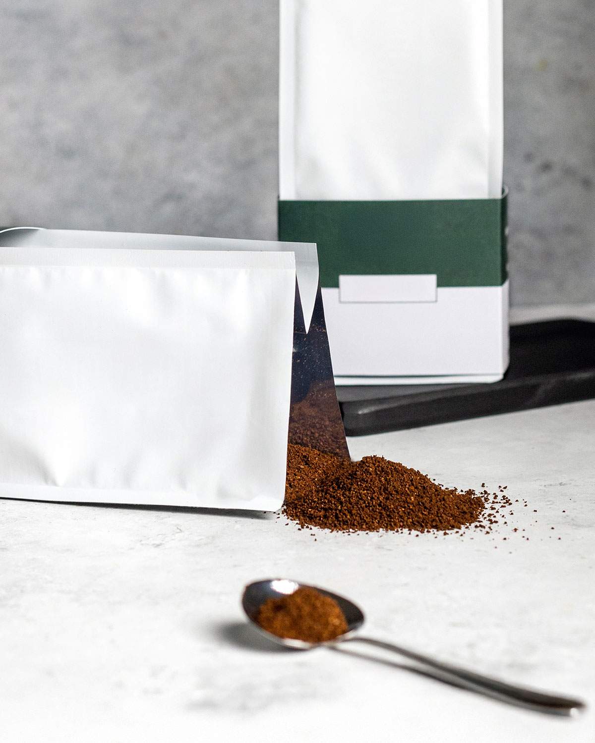 Coffee packaging with coffee grounds spilling from it with a spoon in front.