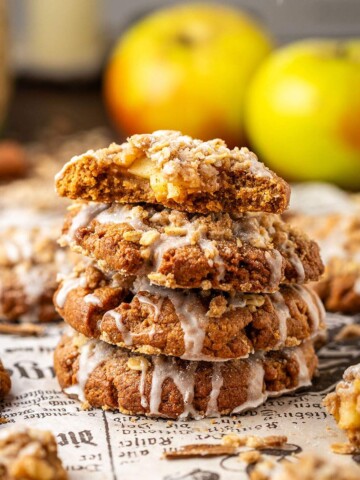 Four stacked apple cookies with glaze, and a bite taken out of the cookie on top, showing the apple filling.