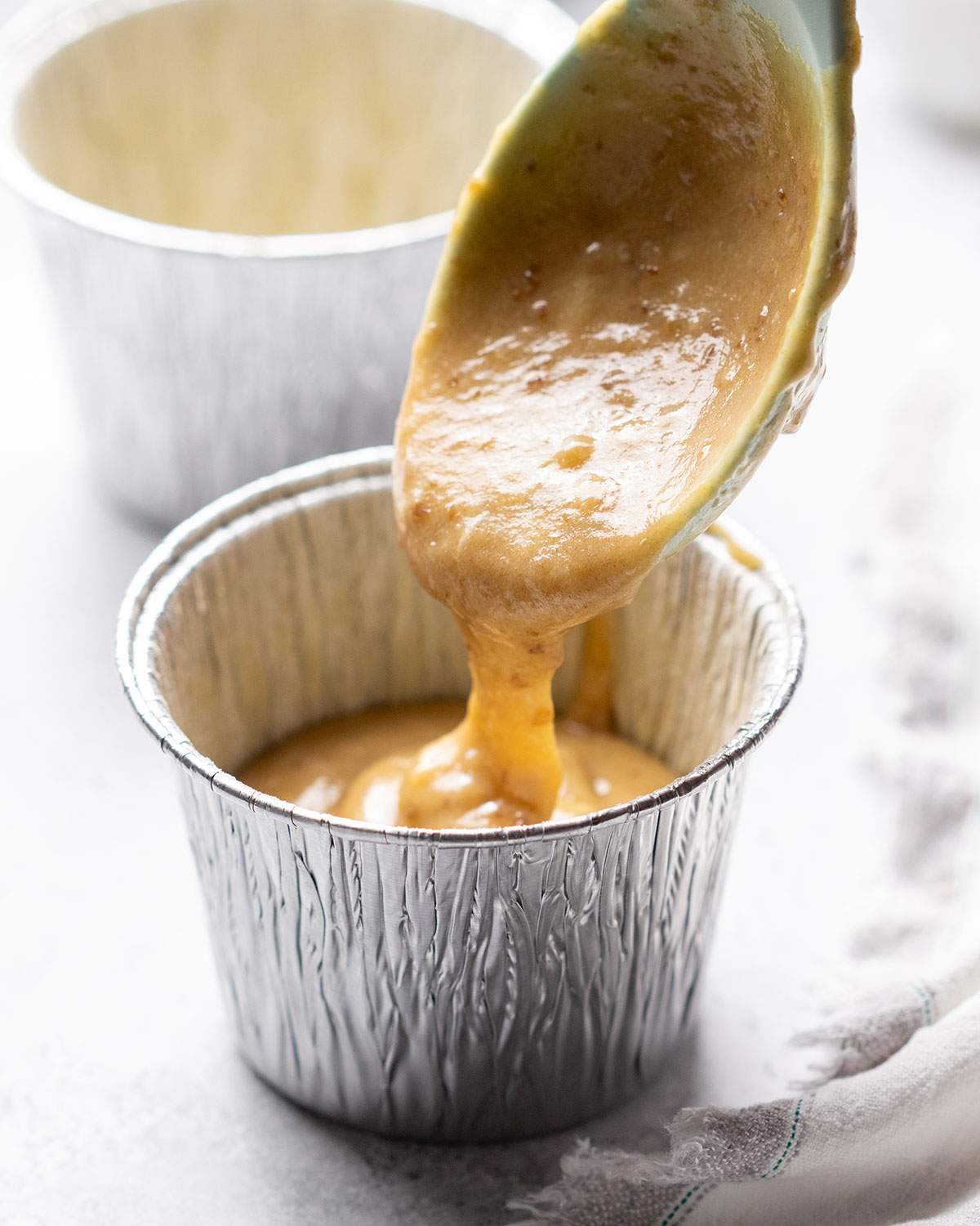Pouring sticky toffee pudding batter into a greased ramekin.