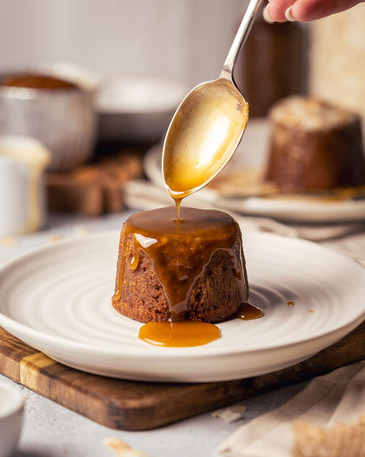 Golden toffee sauce being poured over a sticky toffee pudding.