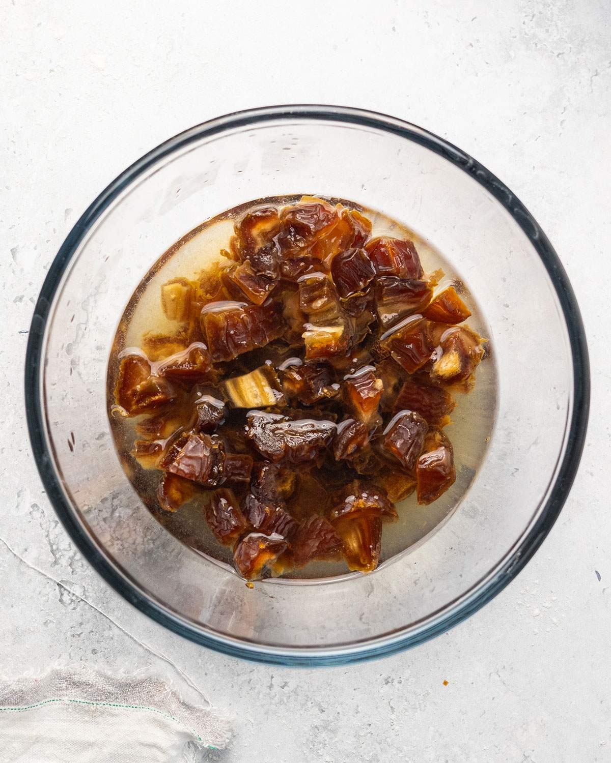 Chopped dates soaking in liquid in a glass bowl.
