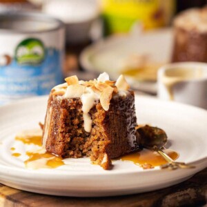 Individual sticky toffee pudding served on a white plate with coconut custard.