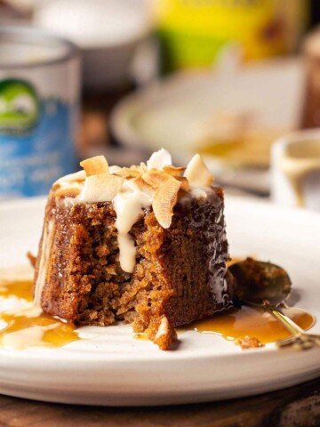 Individual sticky toffee pudding served on a white plate with coconut custard.