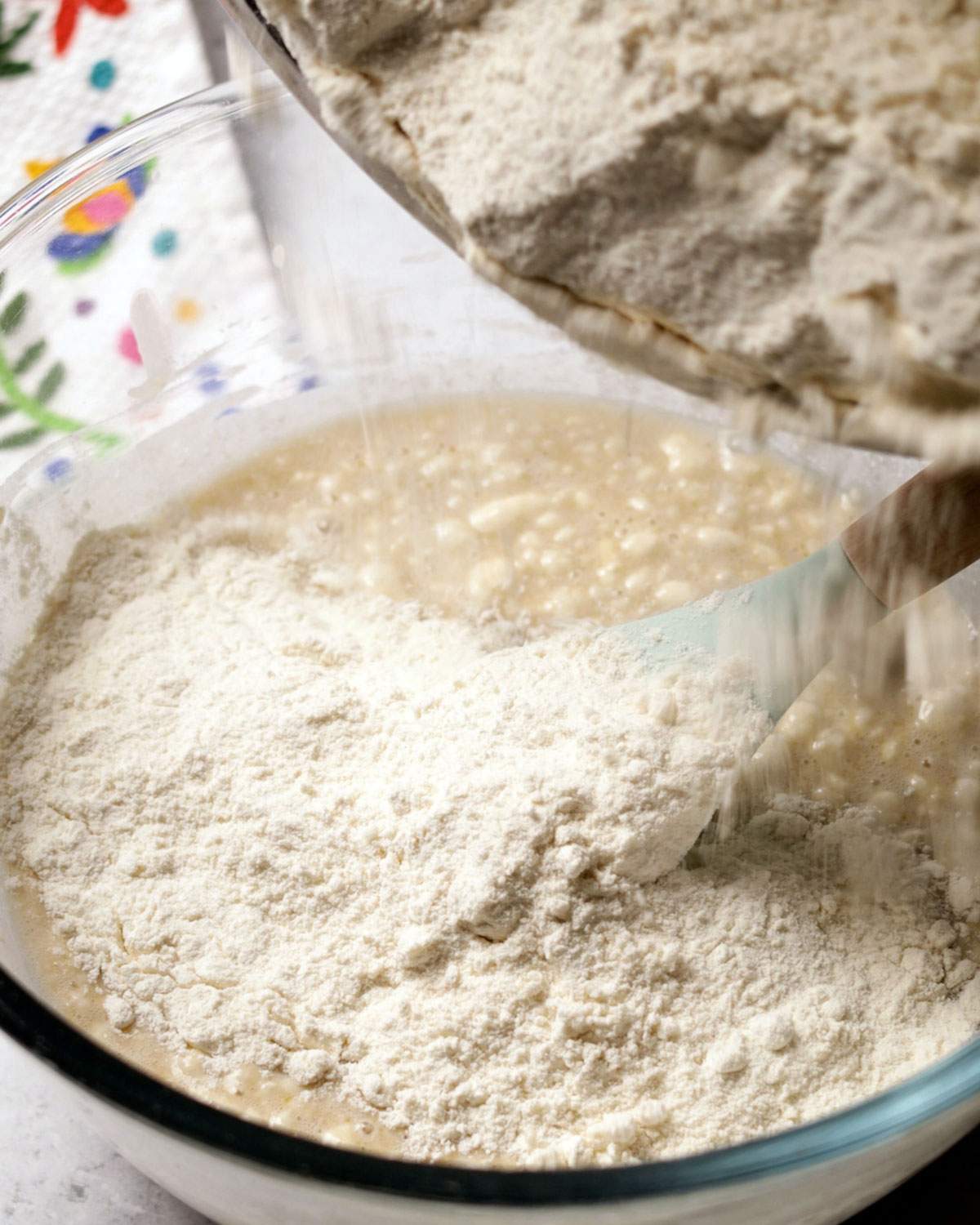 Adding flour to a yeast mixture in a bowl.