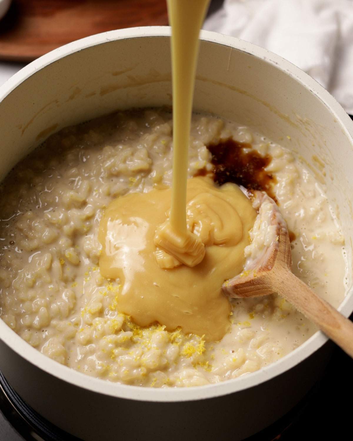 Pouring condensed milk into rice pudding on the stove.