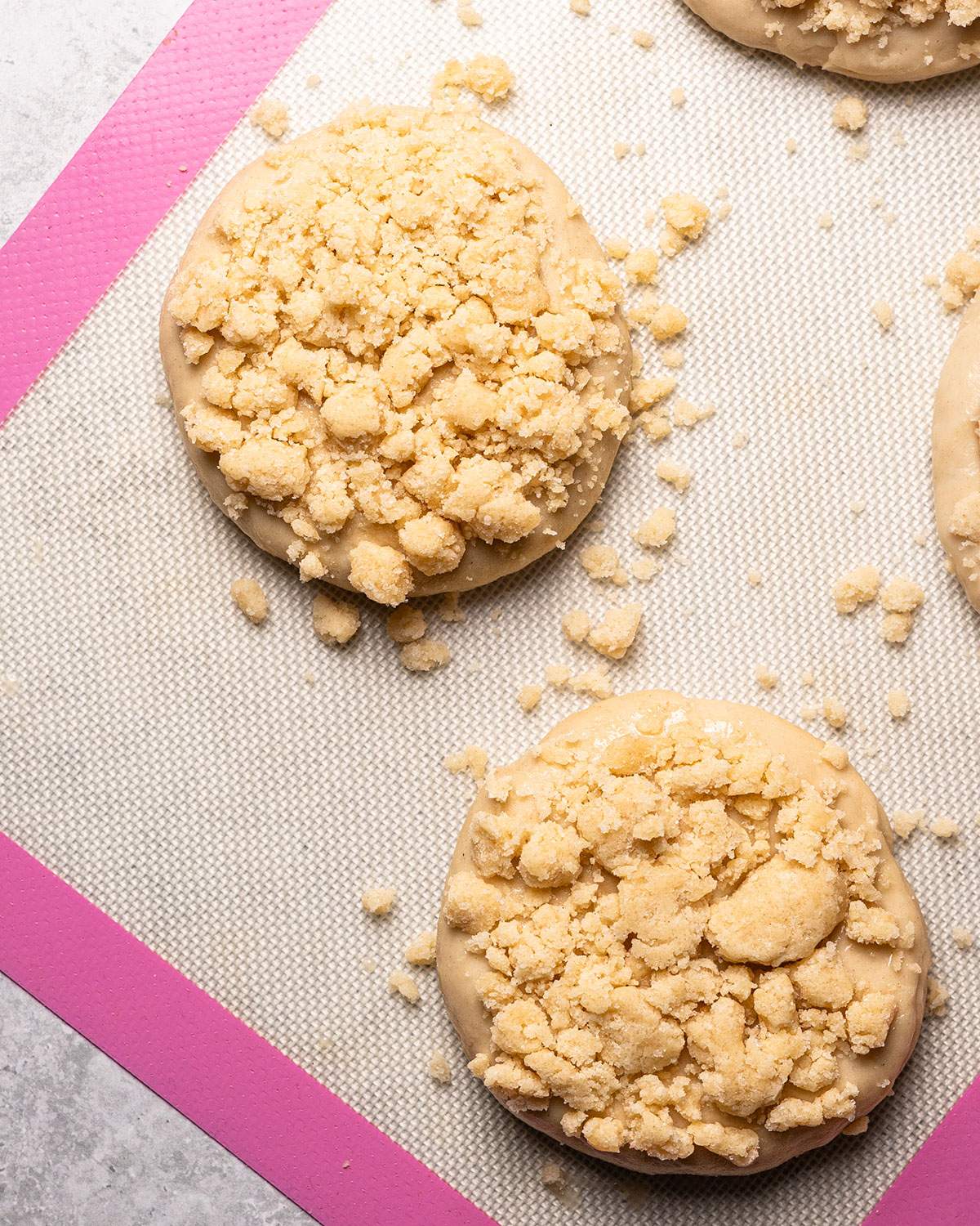 Dough rolls topped with crumble mixture on a baking mat before baking.