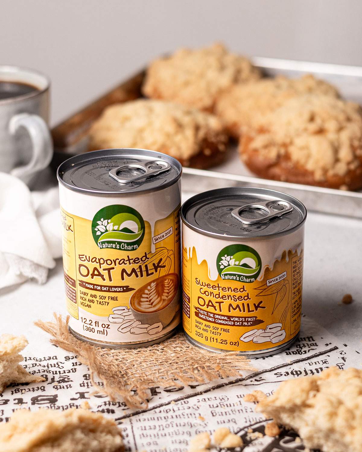 Cans of evaporated oat milk and sweetened condensed oat milk by Nature's Charm on a serving table.