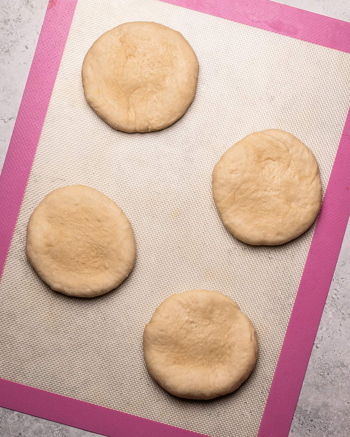 Flattened dough balls on a baking mat.