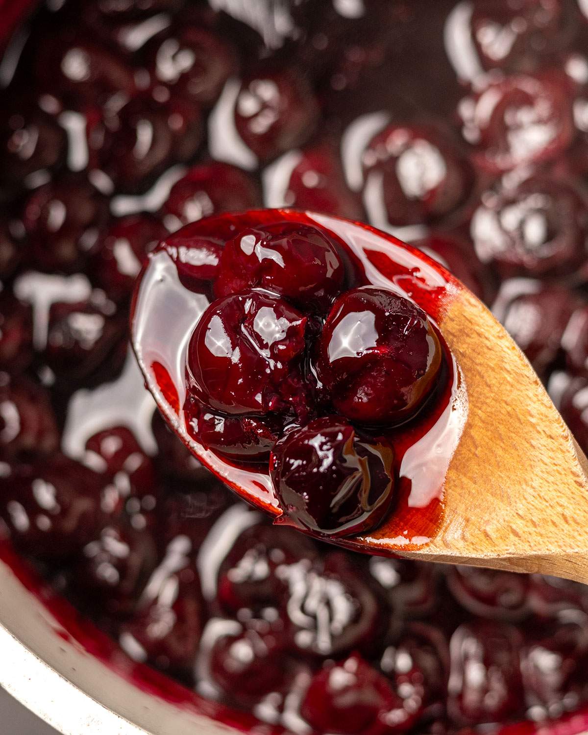 Cherry compote on a wooden spoon above saucepan.