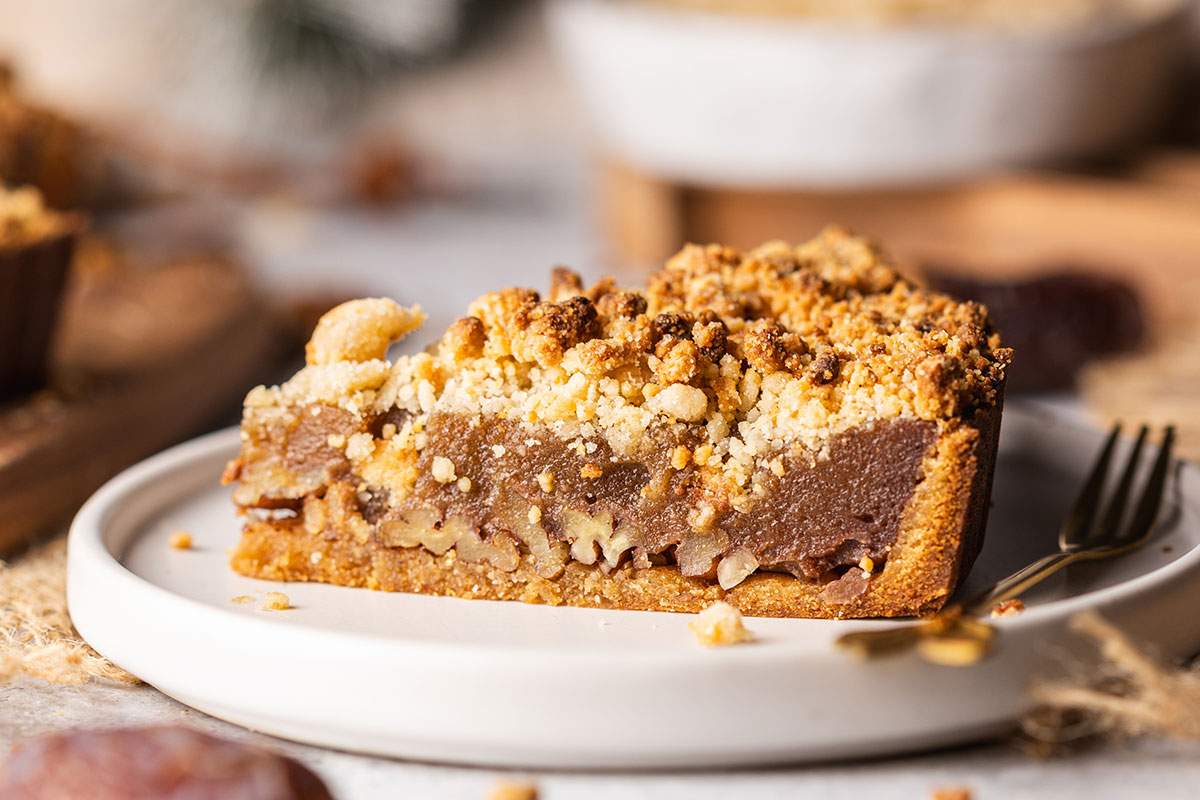 Vegan date caramel tart with pecan crumble topping on white plate.