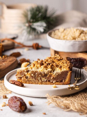 Vegan date caramel pecan tart slice on plate with crumble topping.