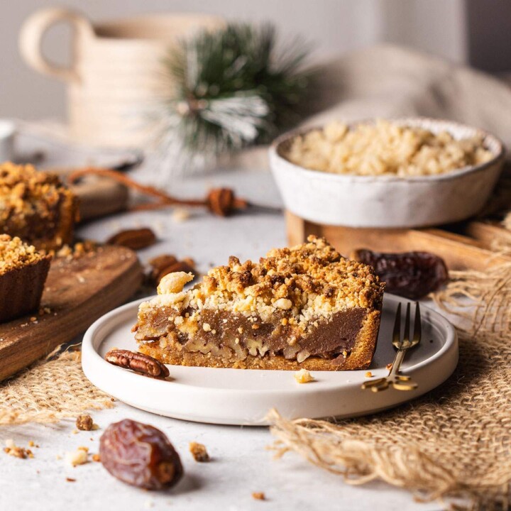 Vegan date caramel pecan tart slice on plate with crumble topping.