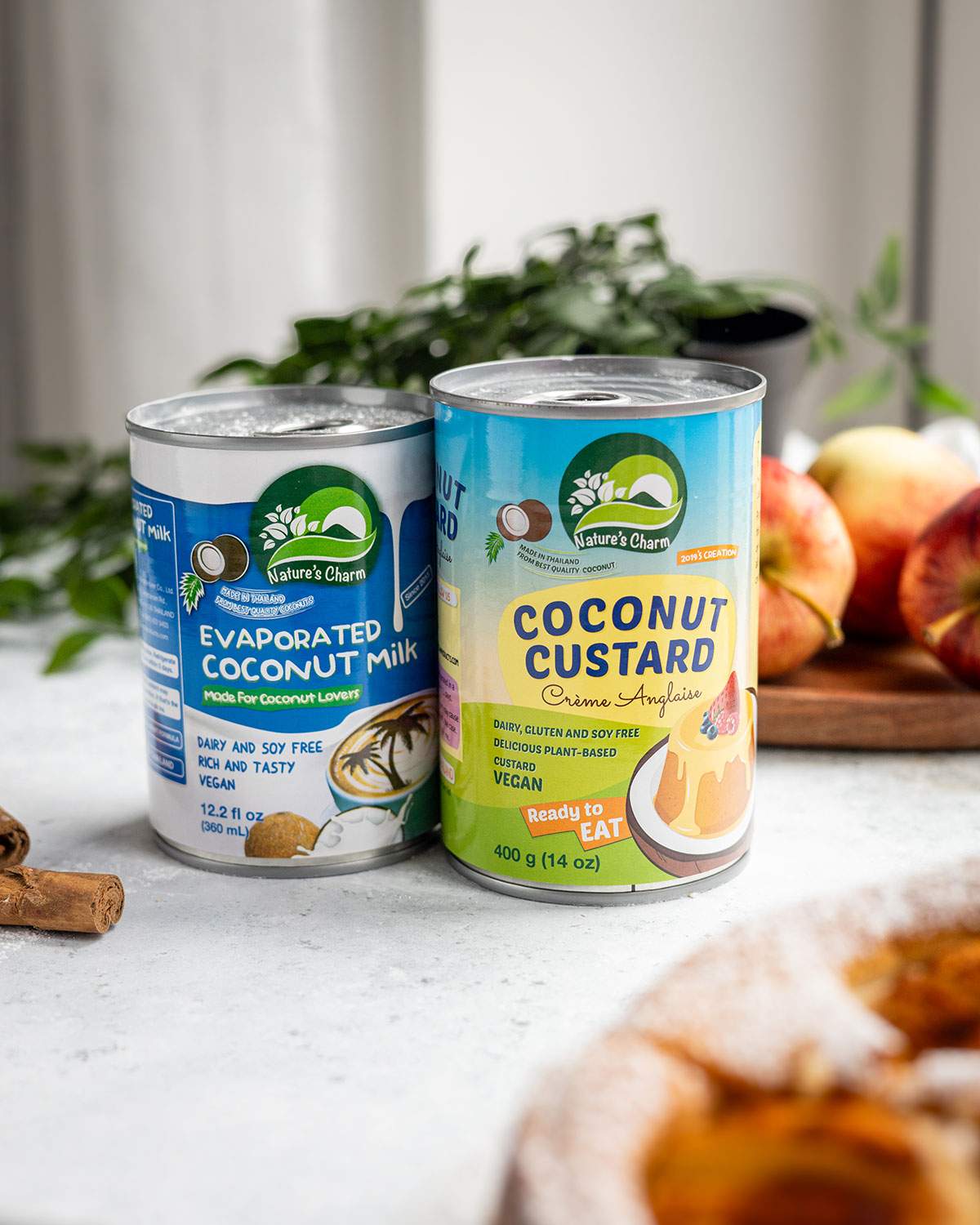 Nature’s Charm evaporated coconut milk and coconut custard cans beside apples and vegan apple cake.